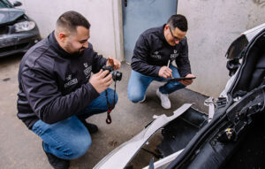Zwei Kfz-Gutachter dokumentieren einen Vorschaden an einem Fahrzeug mit Kamera und Tablet